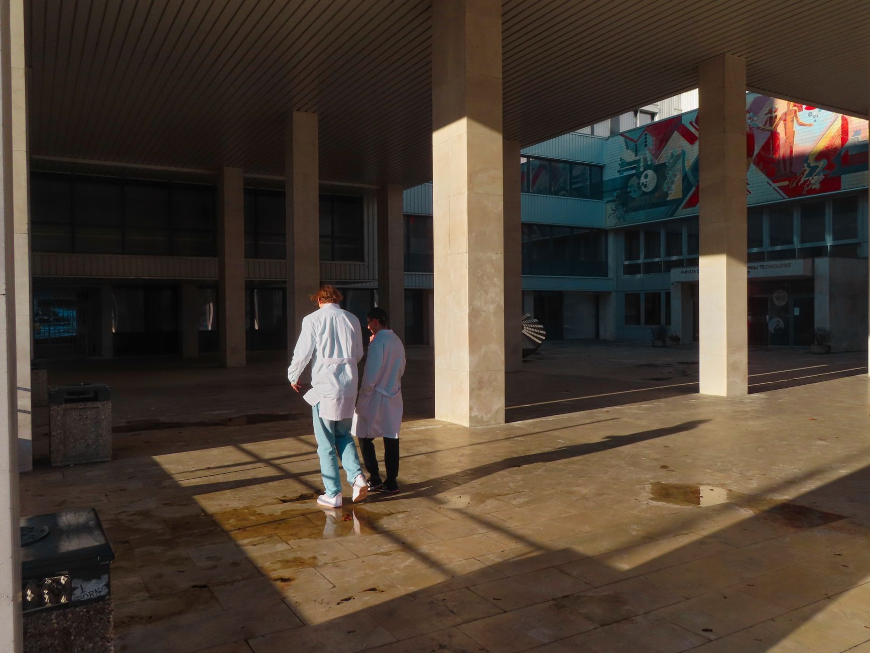 Two doctors in white coats walking through a hospital courtyard