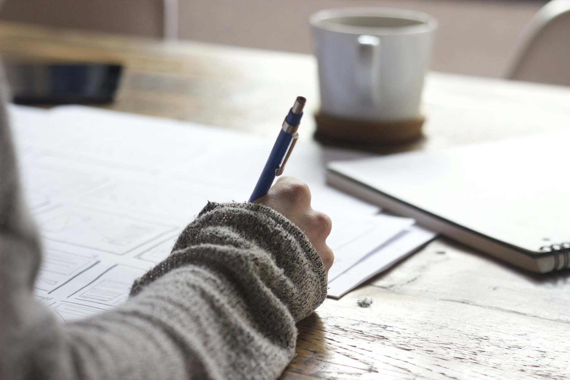 A person making notes over paperwork at a desk with a coffee
