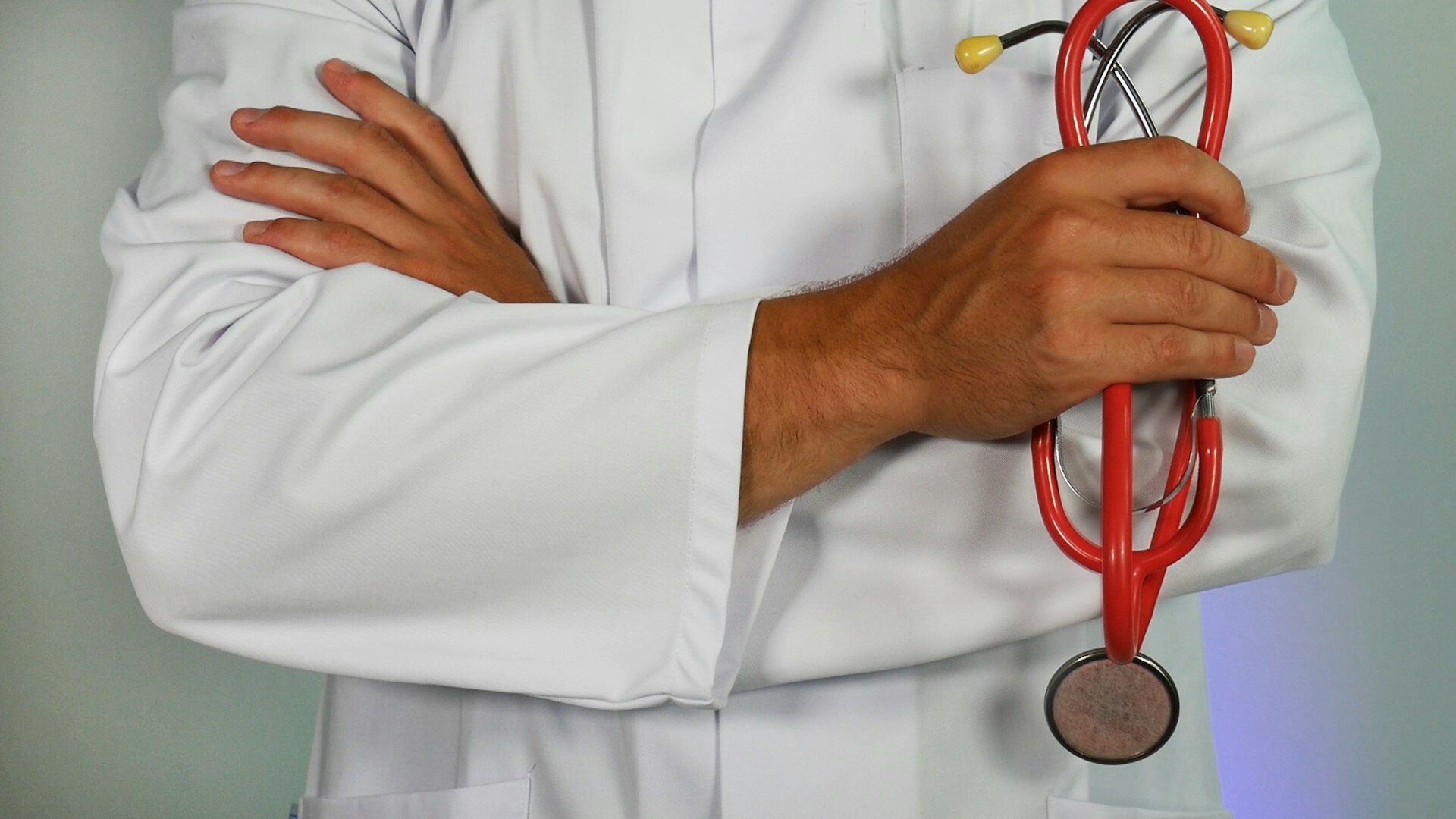 A doctor in a white coat holding a stethoscope, arms folded