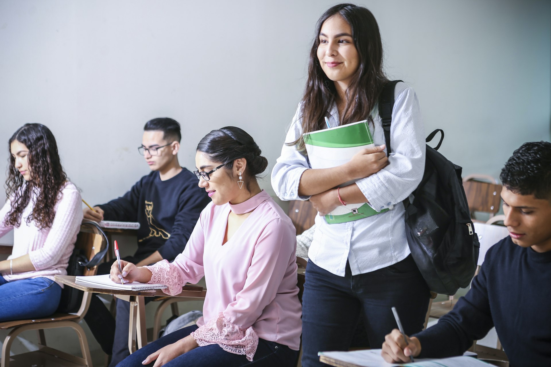 Students taking notes in a lecture room, one standing with a notebook