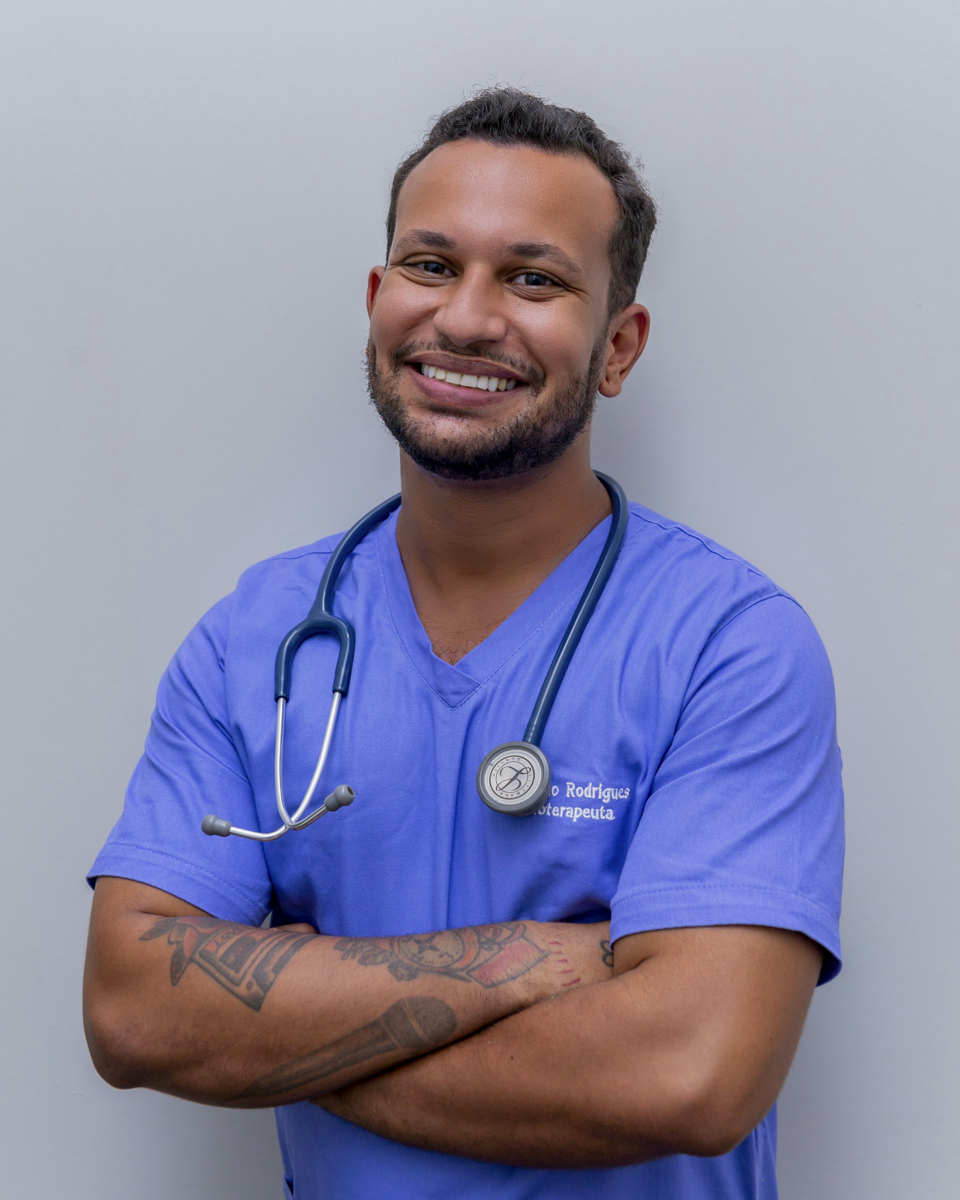 A physician in blue scrubs with a stethoscope, smiling